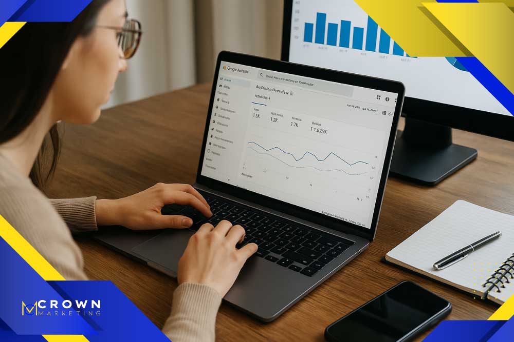 A person analyzes Google Analytics on a laptop, reflecting Crown Marketing's SEO Las Vegas expertise. A pen, notebook, and smartphone rest on the wooden table.| Crown Marketing Digital Marketing Agency Las Vegas