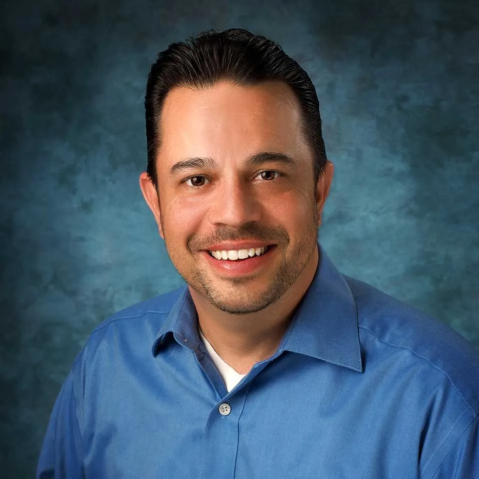 A smiling man in a blue shirt against a textured blue background, representing Crown Marketing's digital marketing services expertise.| Crown Marketing Digital Marketing Agency Las Vegas