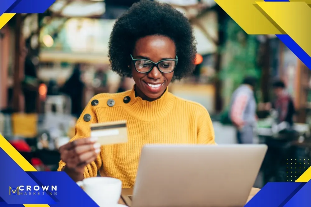 A woman in a yellow sweater shops online with a credit card and laptop, representing Crown Marketing's digital marketing services expertise in enhancing online sales.| Crown Marketing Digital Marketing Agency Las Vegas